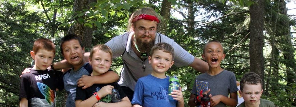 six kids and their counselor pose for a photo in the woods