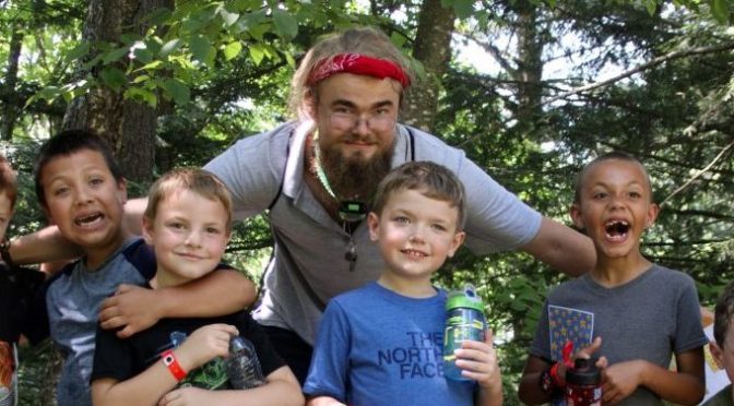 six kids and their counselor pose for a photo in the woods